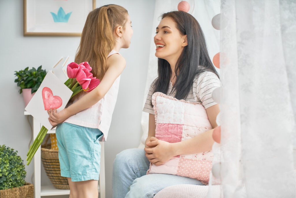 Gelukkige moederdag! Kind dochter feliciteert moeder en geeft haar bloemen tulpen. Mama en meisje die glimlachen en omhelzen. Familievakantie en samenhorigheid.